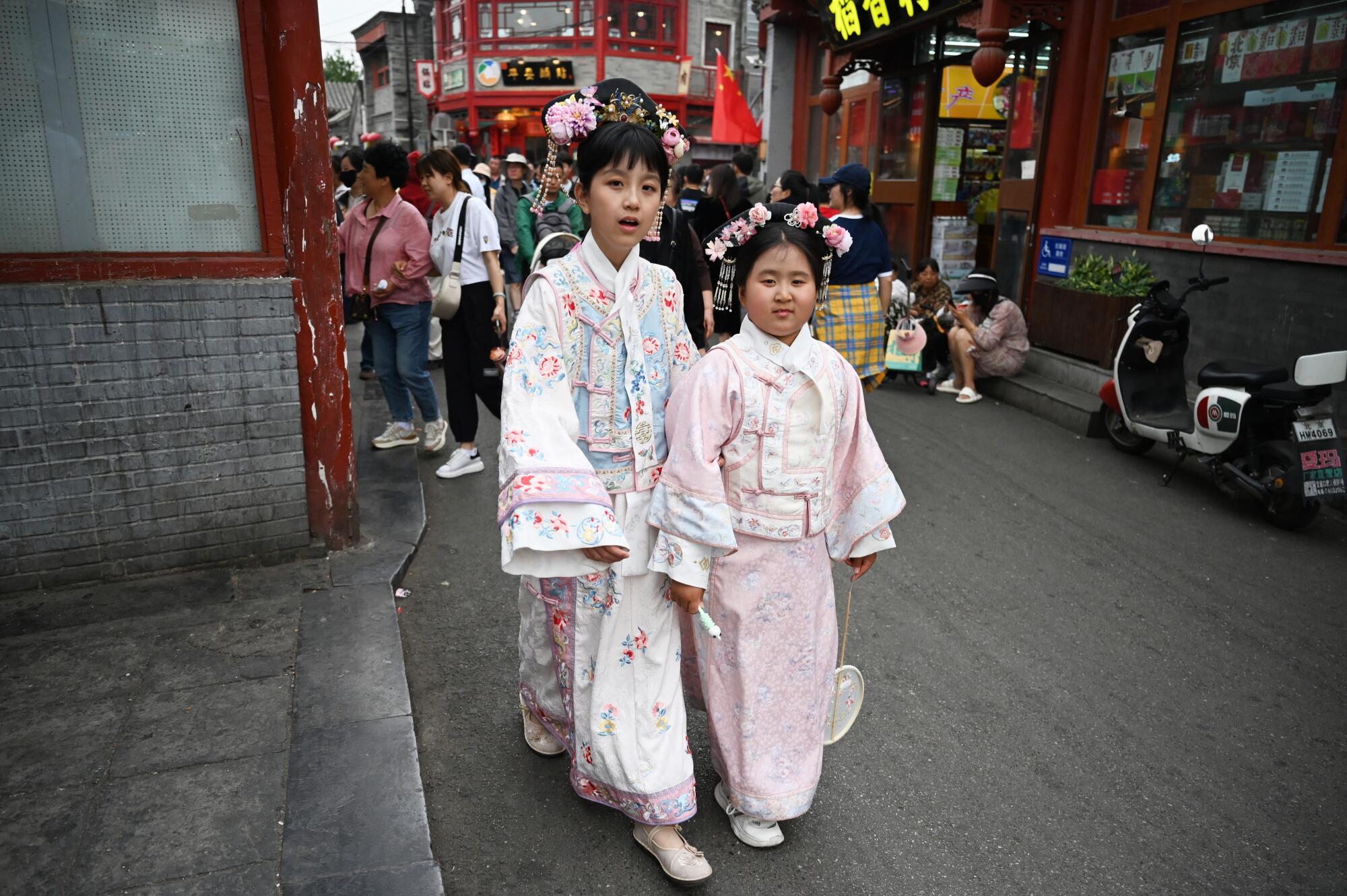 Duas meninas vestindo vestes tradicionais em tons pastéis caminham em uma área comercial turística