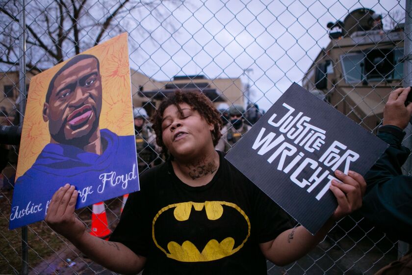 BROOKLYN CENTER, MN - APRIL 14: A demonstrator reacts along a perimeter fence guarded by police during a protest decrying the shooting death of Daunte Wright, while also holding a rendering of George Floyd, outside the Brooklyn Center Police Department, Wednesday, April 14, 2021, in Brooklyn Center, Minn. (Jason Armond / Los Angeles Times)