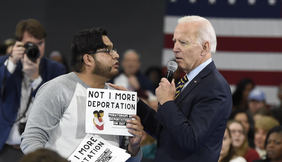 Joe Biden puts his arm on the shoulder of a protester who holds a sign: "Not 1 more deportation."