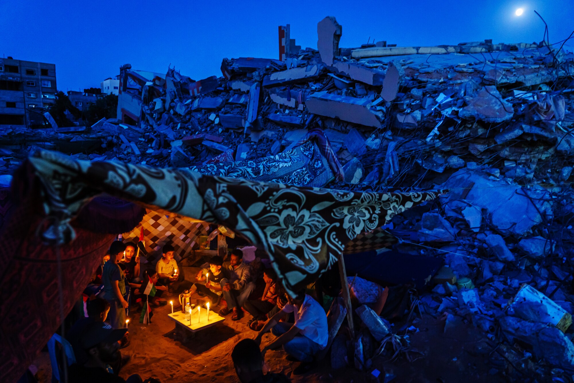 Palestinian families huddle amid the rubble to attend a candlelight vigil in Gaza City.
