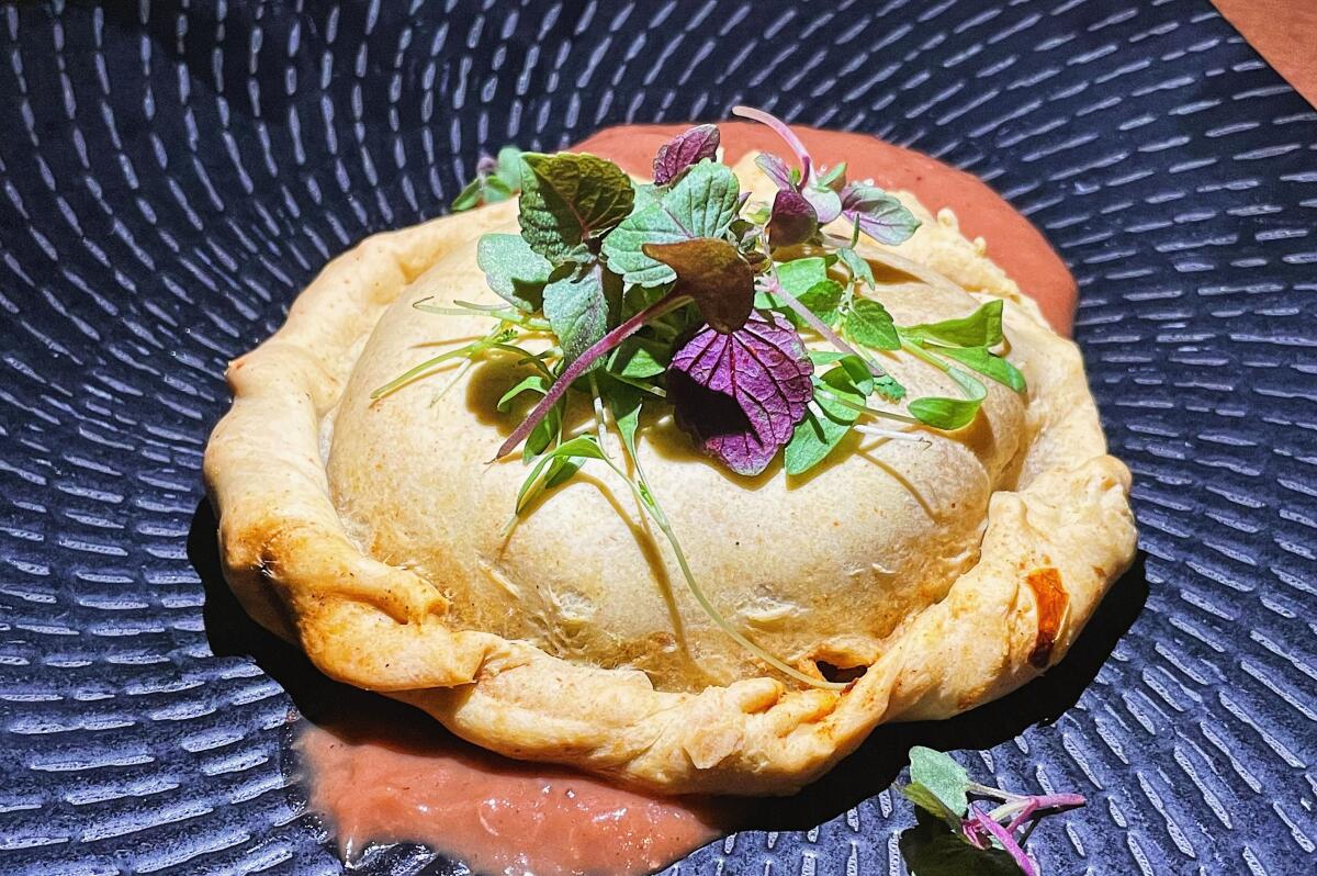 A lion's mane pie atop pink tamarind apple sauce on a black plate, topped with fresh herbs