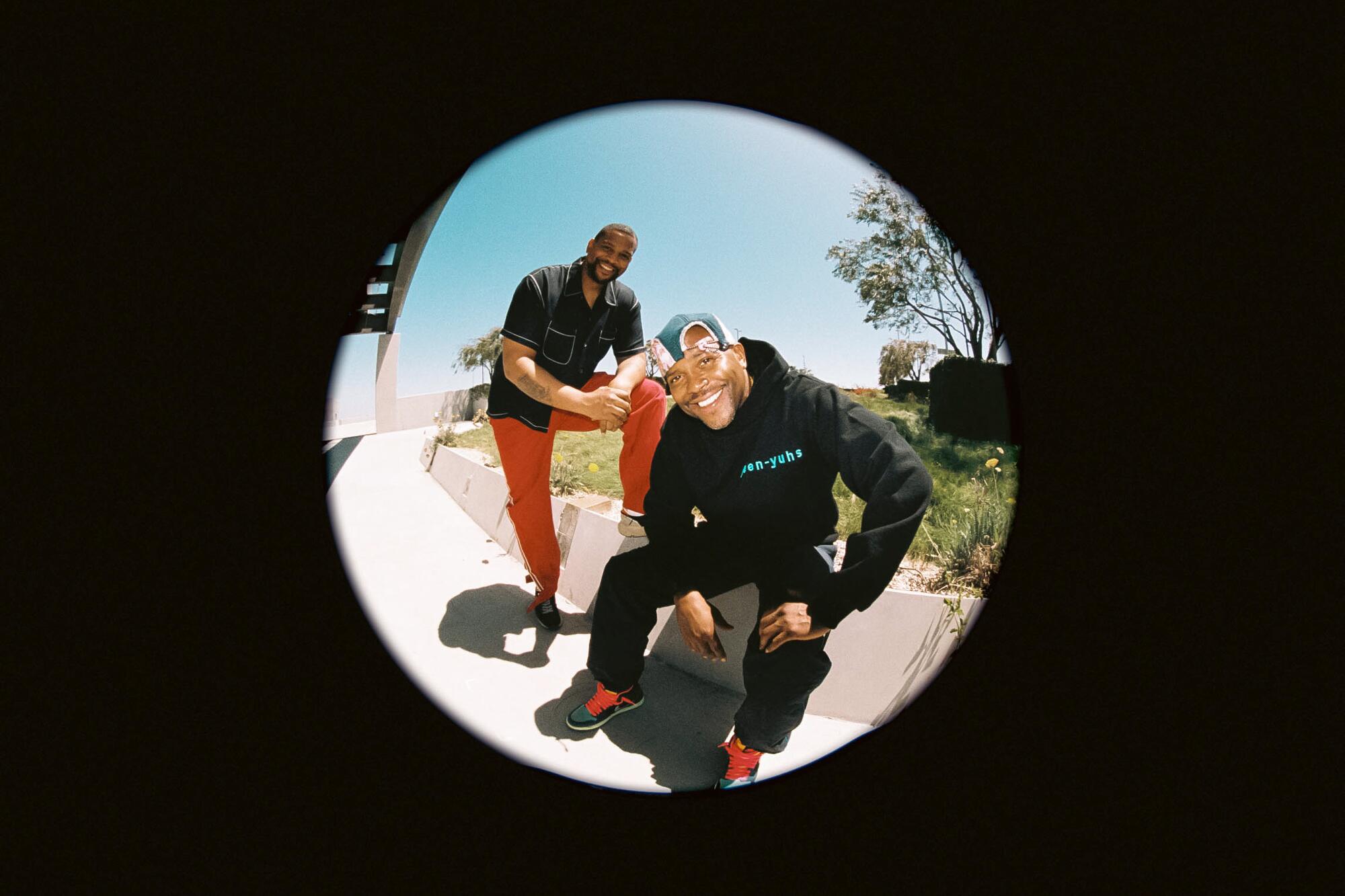 Two men pose for a portrait in a circle of light surrounded by black.