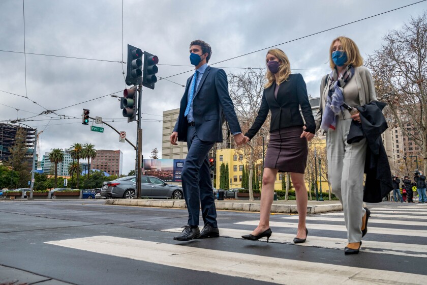 Elizabeth Holmes crosses a street holding hands with her partner and her mother