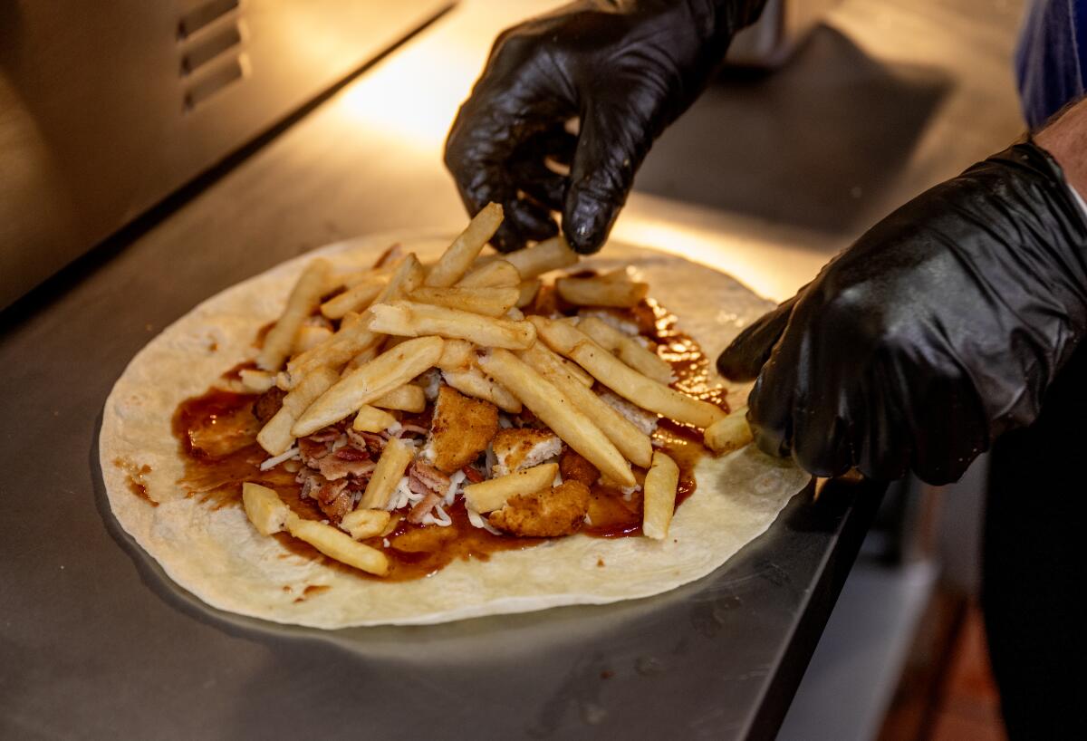 Gloved hands prepare a French taco 