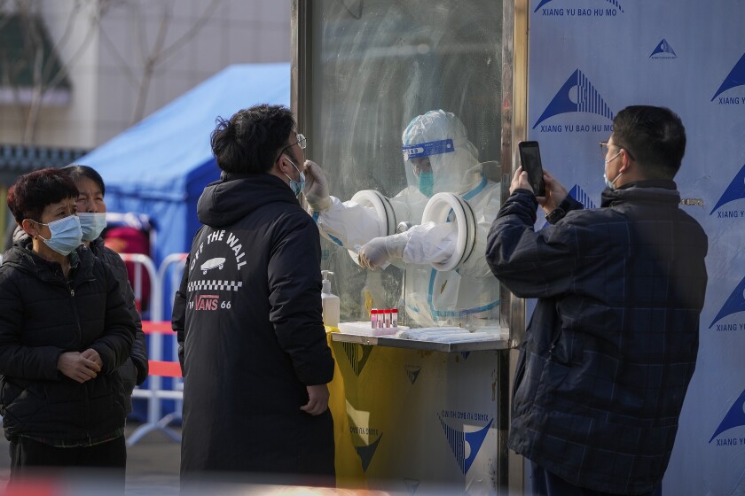 Un hombre usa un teléfono celular para fotografiar a los vecinos que reciben un hisopado de garganta en un sitio de pruebas para el coronavirus en el distrito Xichen de Beijing, martes 25 de enero de 2022. (AP Photo/Andy Wong)