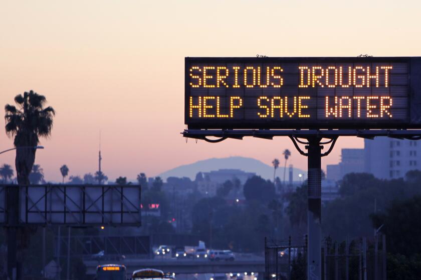 A view of a Los Angeles freeway at dusk, capped by an illuminated sign that reads: SERIOUS DROUGHT. HELP SAVE WATER.