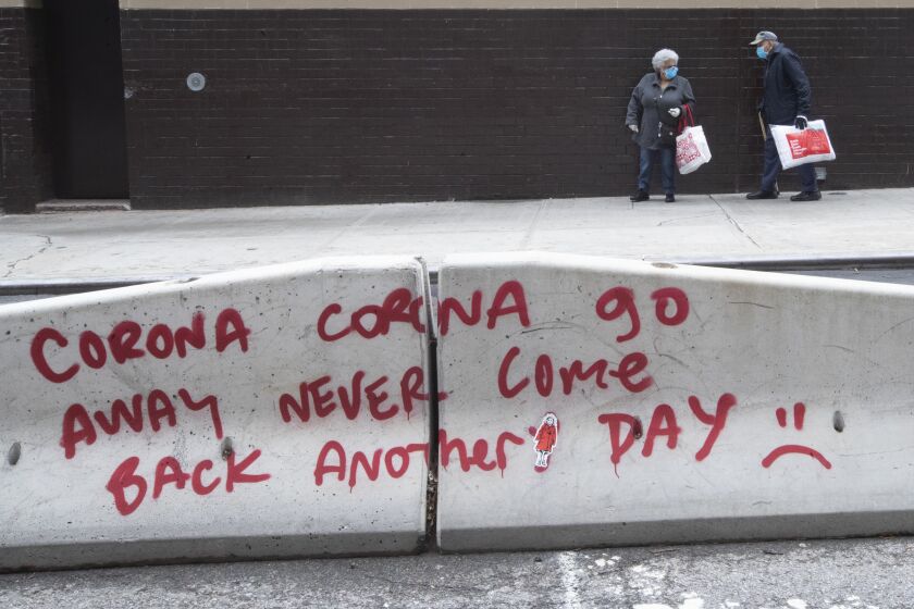 An elderly couple wearing facial masks to protect against the coronavirus walk past graffiti on a street divider calling on the coronavirus to go away, Monday, May 11, 2020, in on the Lower East Side of Manhattan. (AP Photo/Mary Altaffer)