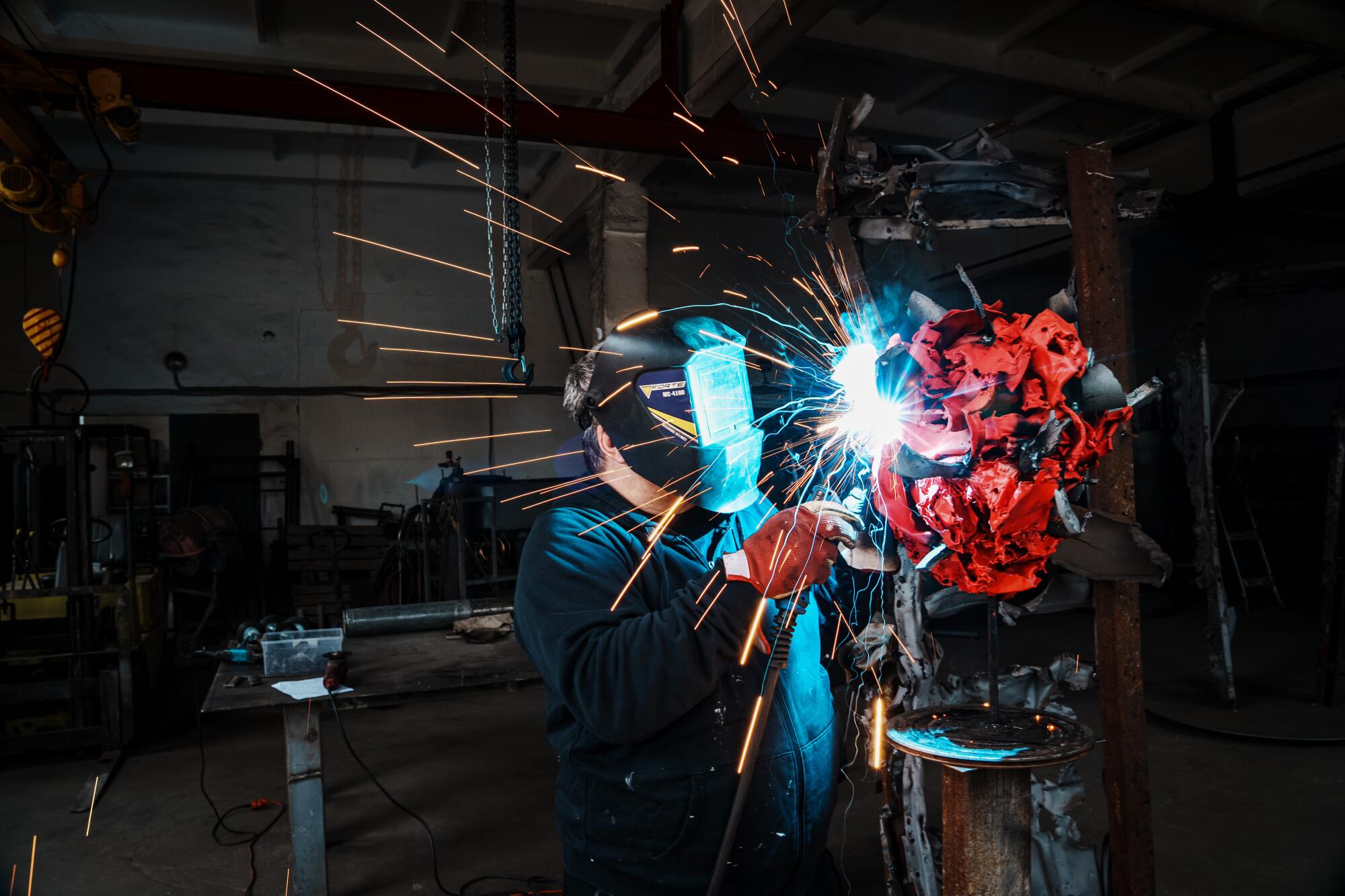 Sparks fly as Reva, in a welding mask, melds and transforms war debris into artworks.