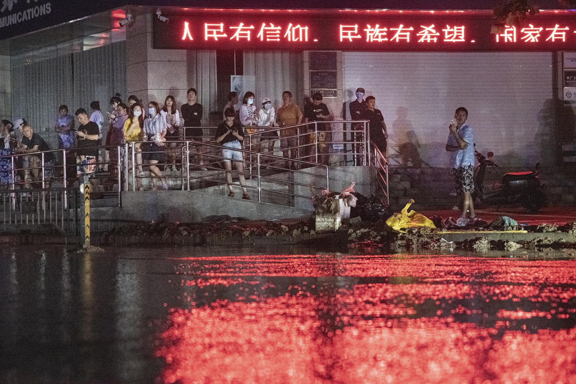 People gather outside a building under a neon sign with Chinese characters 