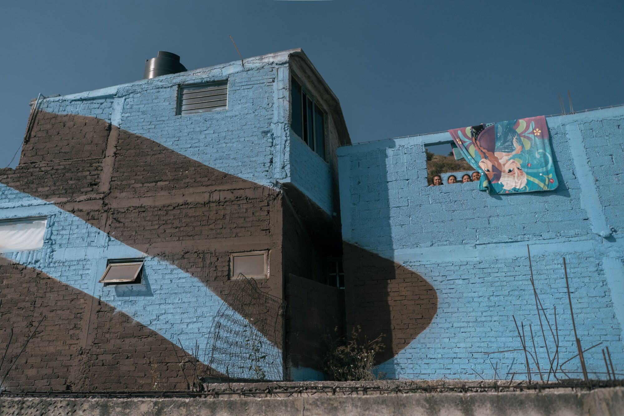 Four people look out of an upstairs opening in their home, which painted in blue with black stripes 