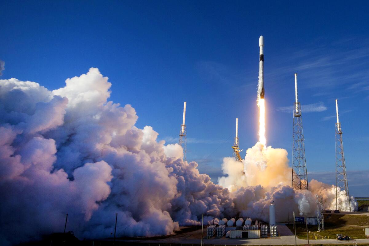 A rocket lifts off, causing clouds of smoke among towers.