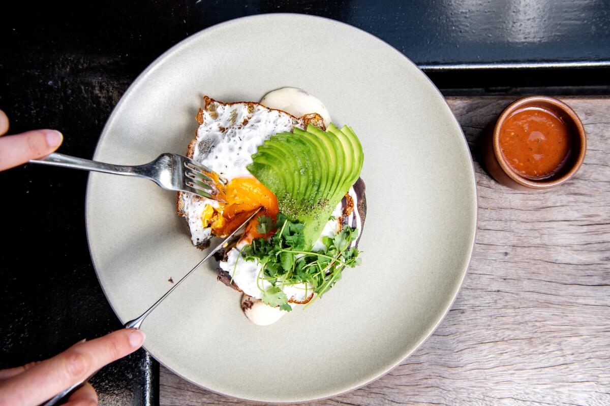 Digging into a pupusa dish with mushroom, avocado, black crema, salsa roja and  fried egg. 