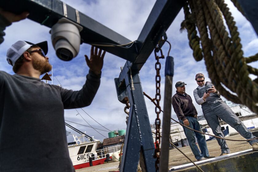 Mark Hager, left, positions a camera with the help of Anthony Lucia, right, as captain Al Cottone watches the feed on a monitor from his boat, the Sabrina Maria, in Gloucester, Mass., May 11, 2022. Hager's Maine-based startup, New England Maritime Monitoring, is one of a bevy of companies seeking to help commercial vessels comply with new federal mandates aimed at protecting dwindling fish stocks. But taking the technology overseas, where the vast majority of seafood consumed in the U.S. is caught, is a steep challenge. (AP Photo/David Goldman)