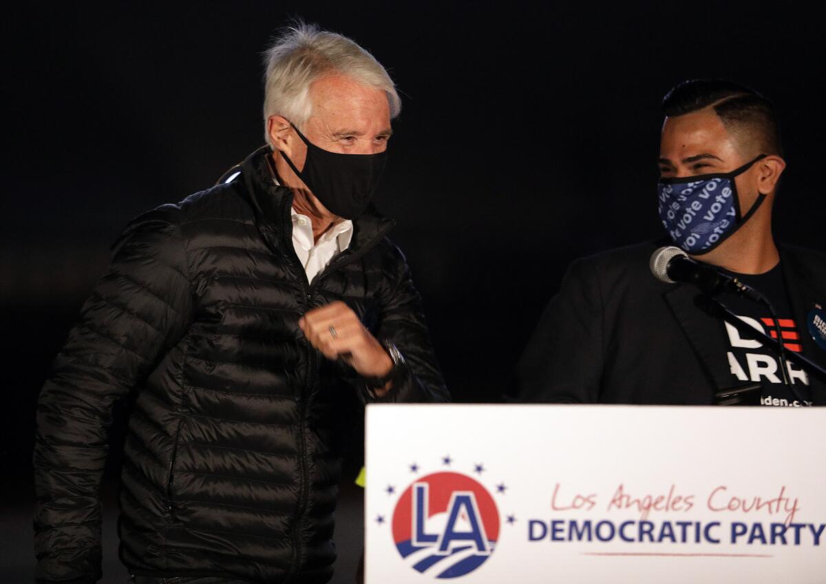 George Gascon, wearing a mask, walks up to a podium with the logo of the Los Angeles County Democratic Party