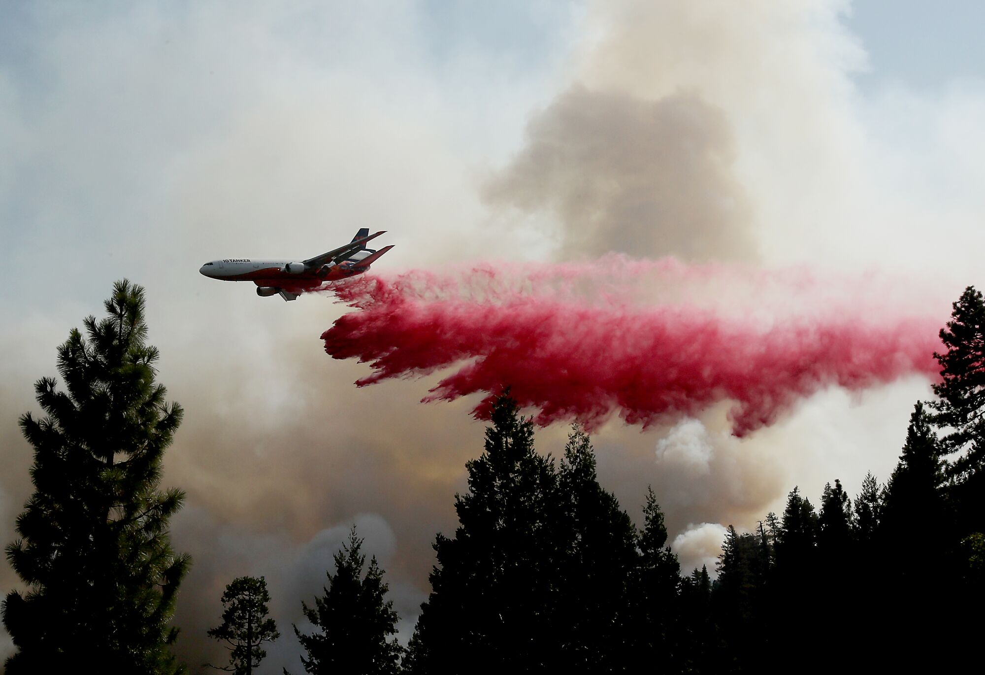 A plane drops red liquid over a burning forest.