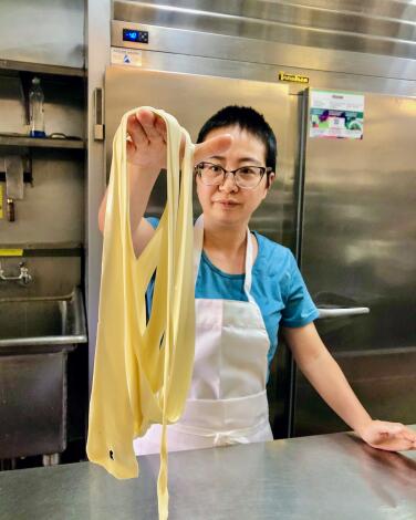 A chef in a restaurant kitchen holds up the biang biang noodle at China Islamic, which is one continuous noodle.