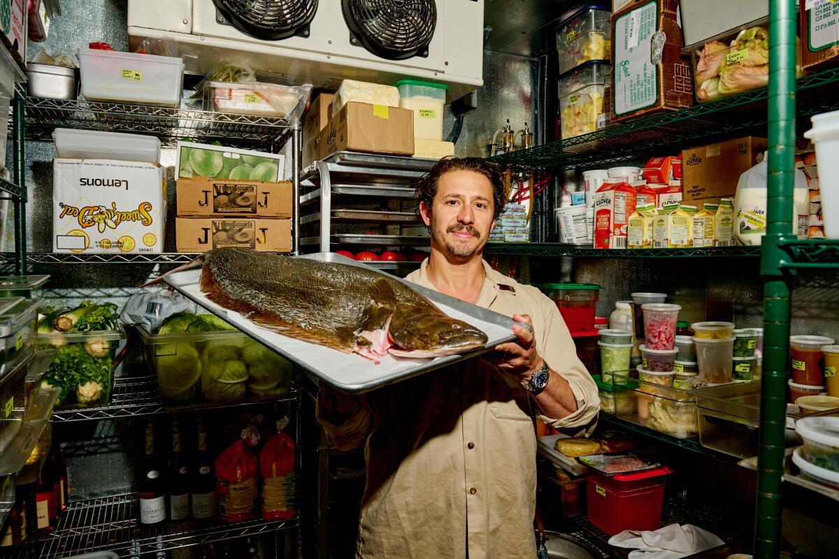A man poses for a photo inside of a refrigerator while holding a halibut