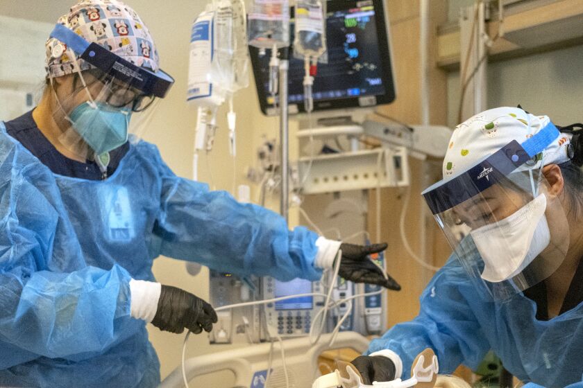 LOS ANGELES, CA - DECEMBER 31: Registered nurse Akiko Gordon, left, and Repertory Therapist Janssen Redondo, right, are working inside the ICU with a covid-19 positive patient at Martin Luther King Jr. Community Hospital (MLKCH) on Friday, Dec. 31, 2021 in Los Angeles, CA. (Francine Orr / Los Angeles Times)