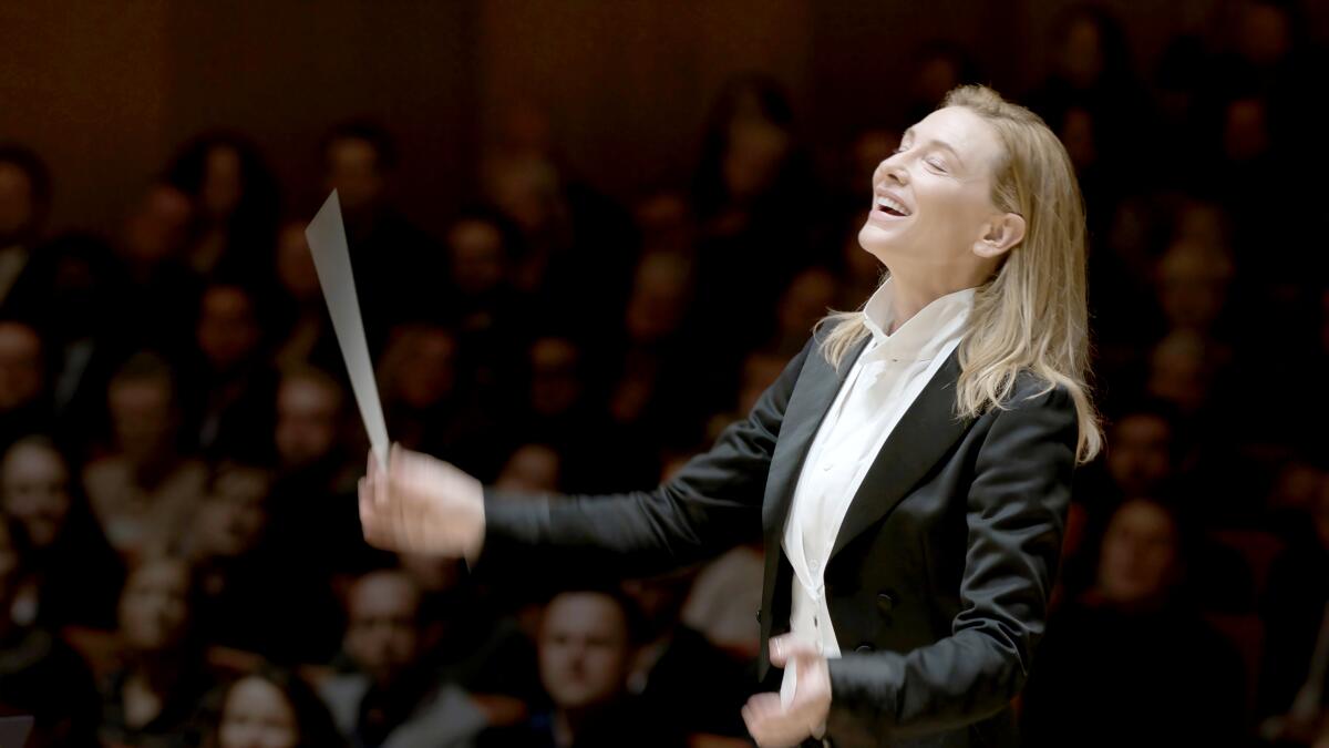 Cate Blanchett, in a black tuxedo, waves an orchestral conductor's baton.