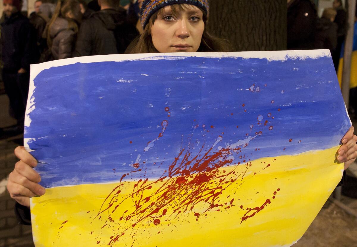 A woman holds an Ukrainian flag with red paint to represent blood in front of the Ukrainian embassy in Warsaw, Poland. Fierce clashes between police and protesters, some including gunfire, shattered a brief truce in Ukraine's besieged capital Thursday, killing numerous people.