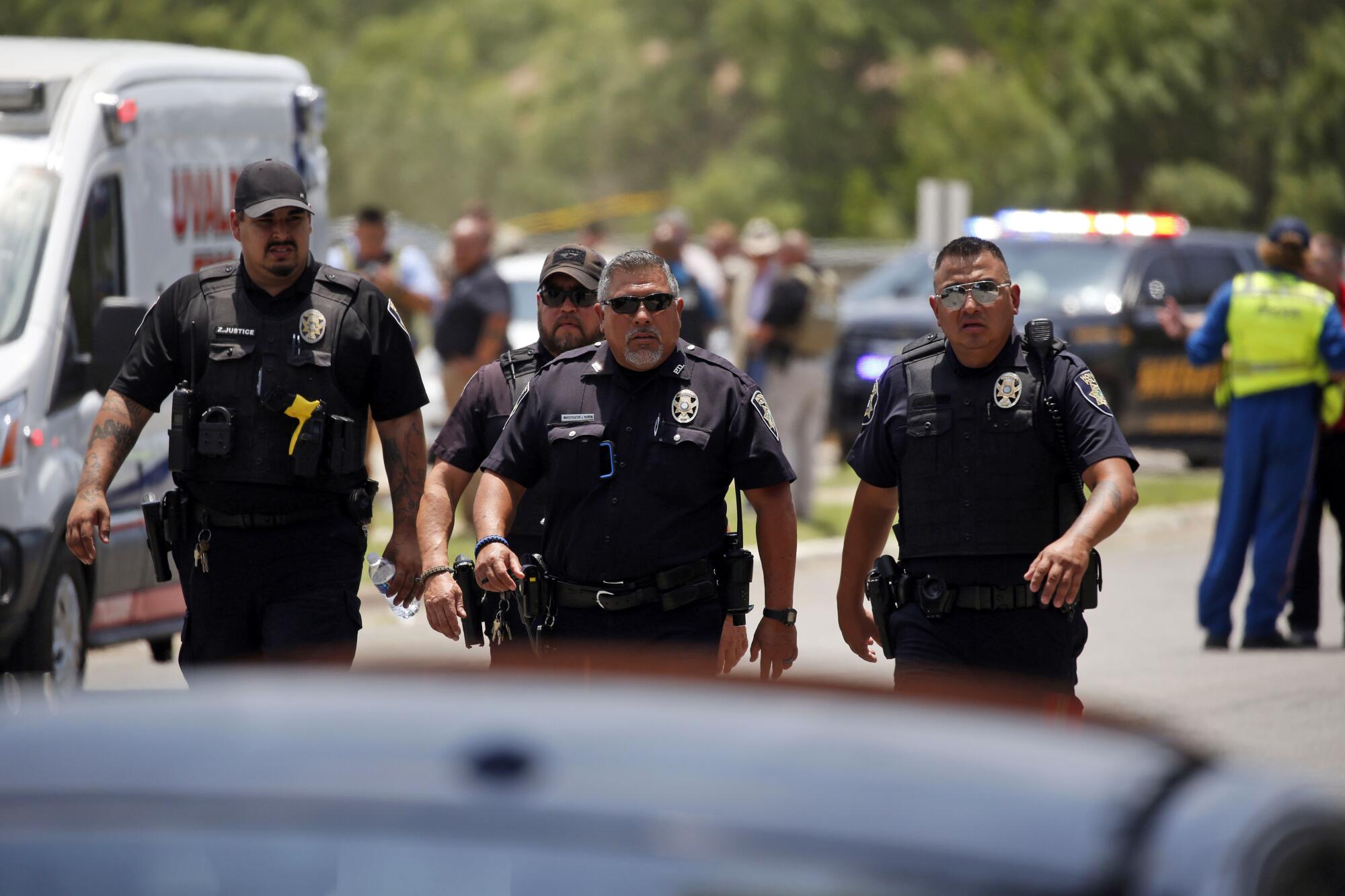 Men in dark police uniforms walk near emergency vehicles