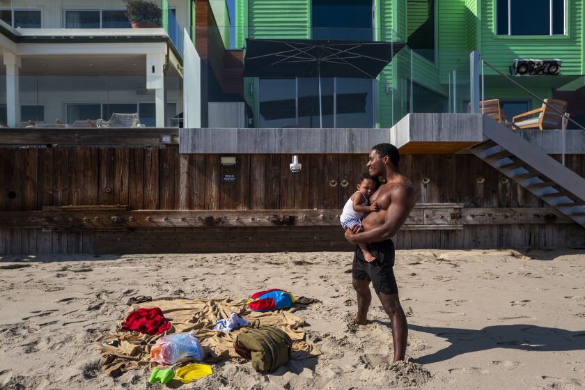 MALIBU, CA - AUGUST 08: Shaun Fury, 29, holds his son Zion Fury, 16 months, on La Costa Beach Sunday, Aug. 8, 2021 in Malibu, CA. They were not camped out close to private homes. After more than 50 years with a sliver of the beach fenced off to the public, local government agencies in May tore down a new illegal fence constructed by Malibu homeowners and opened a short stretch of the beach to the public. The California Coastal Act allows such a move. But after decades of the beach being closed the opening is creating tension with adjacent homeowners. (Francine Orr / Los Angeles Times)