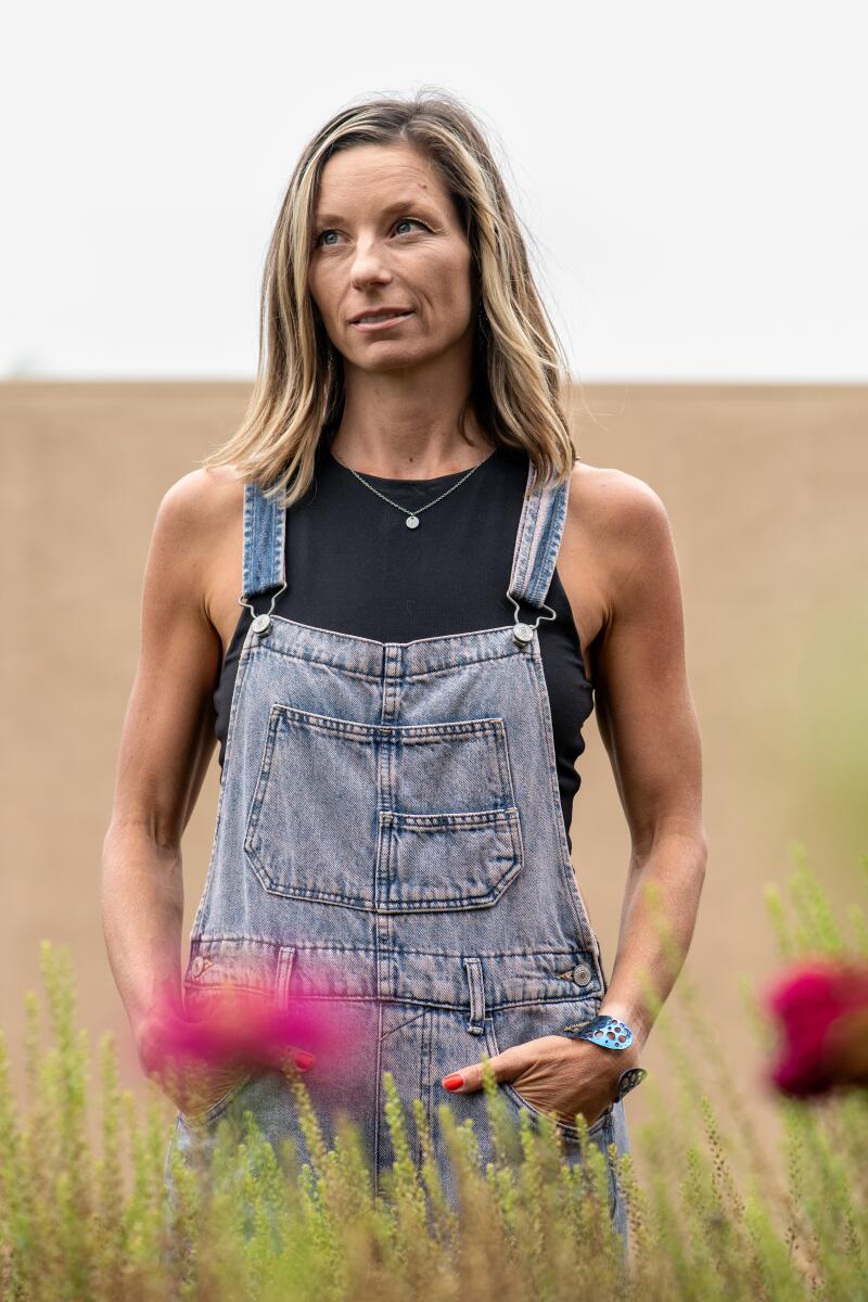 A woman in overalls stands in her flower garden 