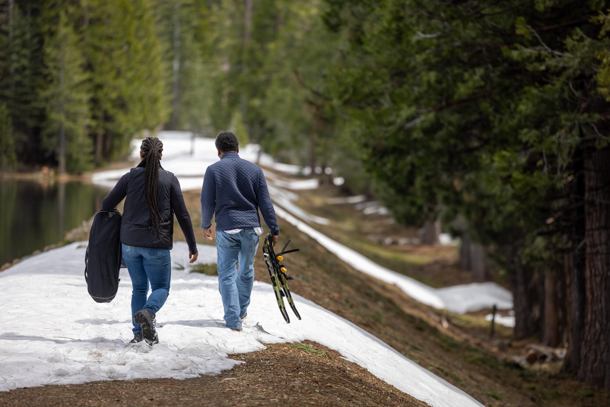 A man and woman walk along a snow-covered earthen dam.