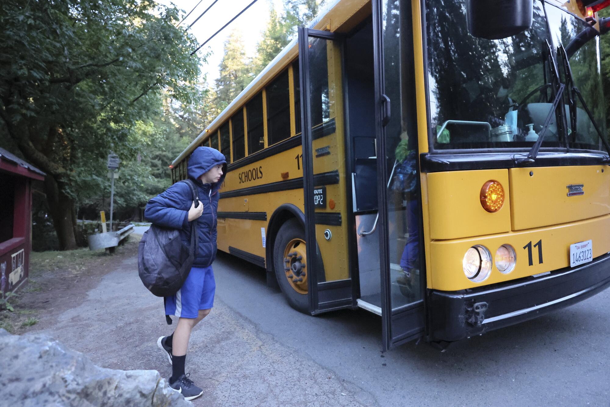 A student walks toward the opened door of a yellow school bus.