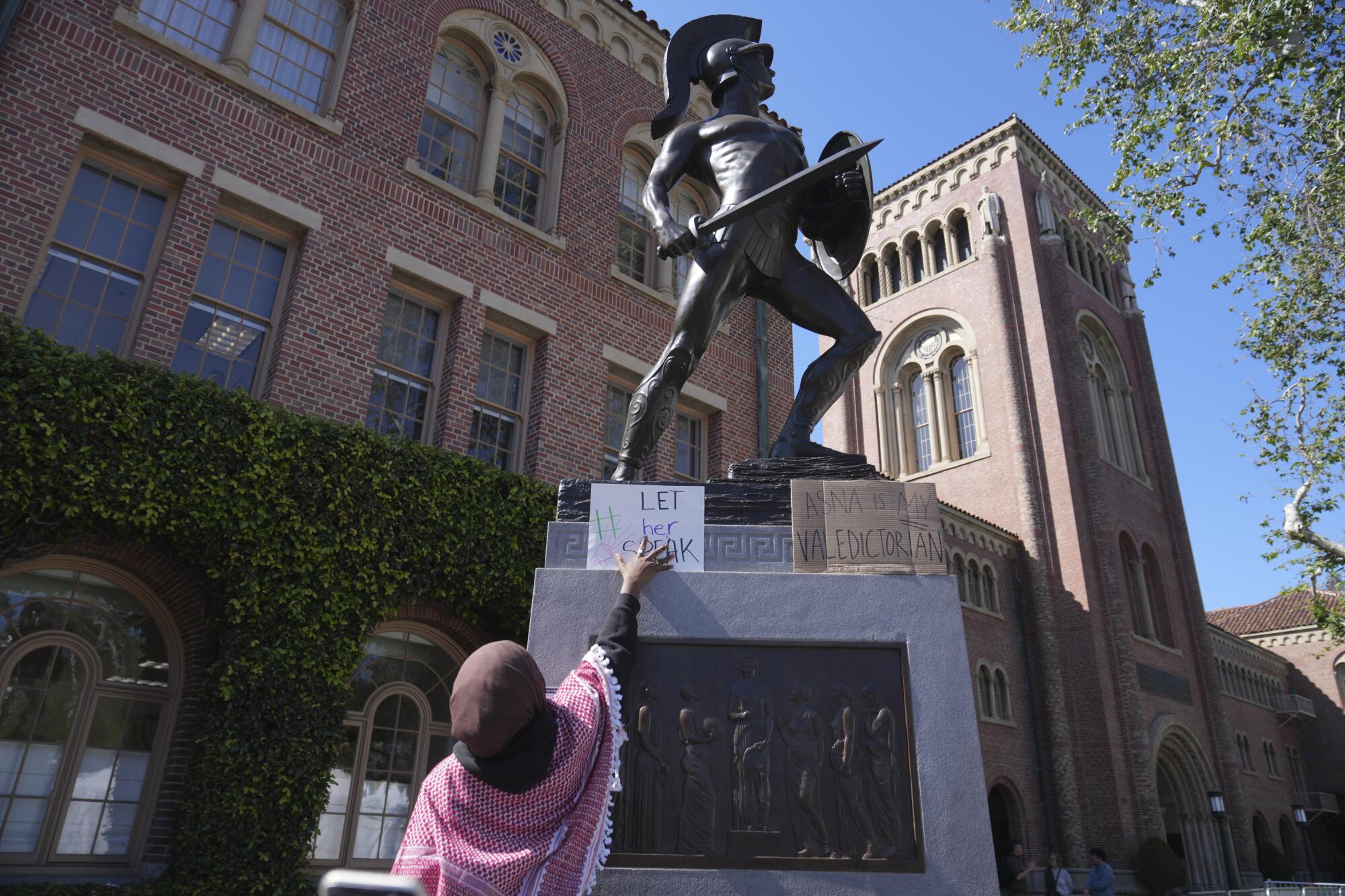 A student places a sign on the Tommy Trojan statue on the USC campus.