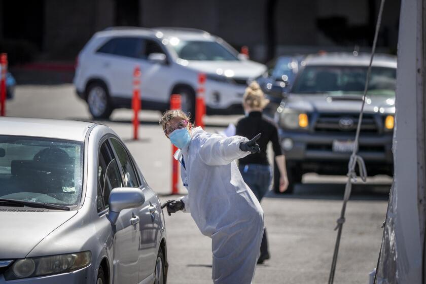 WESTMINSTER, CA -- WEDNESDAY, APRIL 8, 2020: Healthcare workers tend to a driver in line at a drive-through Coronavirus (COVID-19) testing site at the Westminster Mall in Westminster, CA, Wednesday, April 8, 2020. The site is run by Elevated Health and is doing nasal testing for $125 and antibody testing for $75. (Allen J. Schaben / Los Angeles Times)