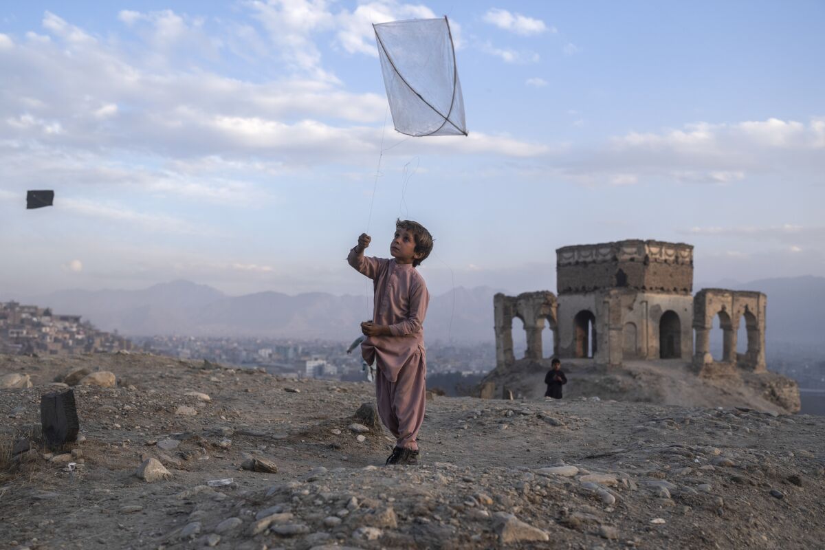 A boy flies a kite on a treeless hill with the ruins of an old building in the background