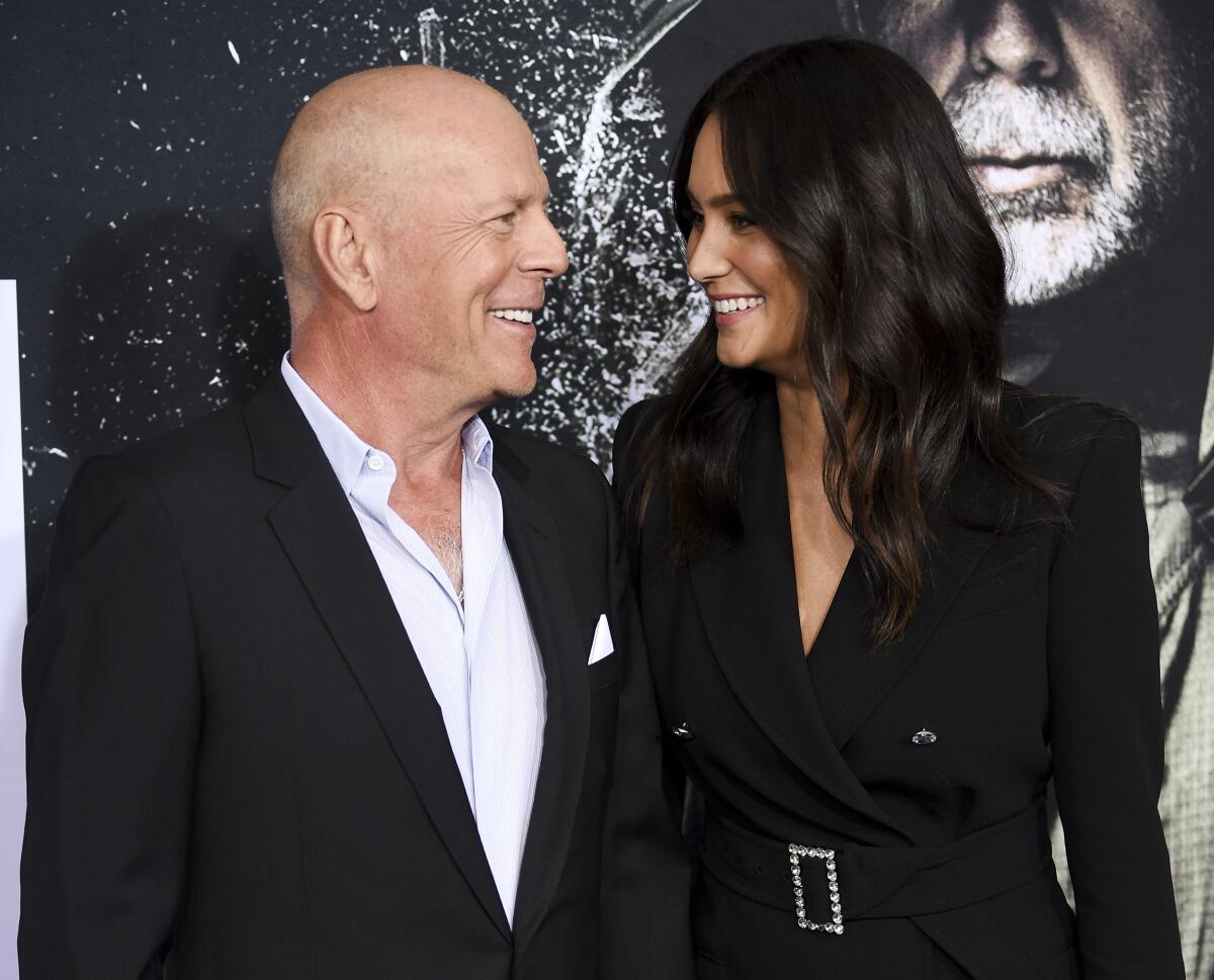 Bruce Willis and Emma Heming Willis smiling at each other while wearing black suits