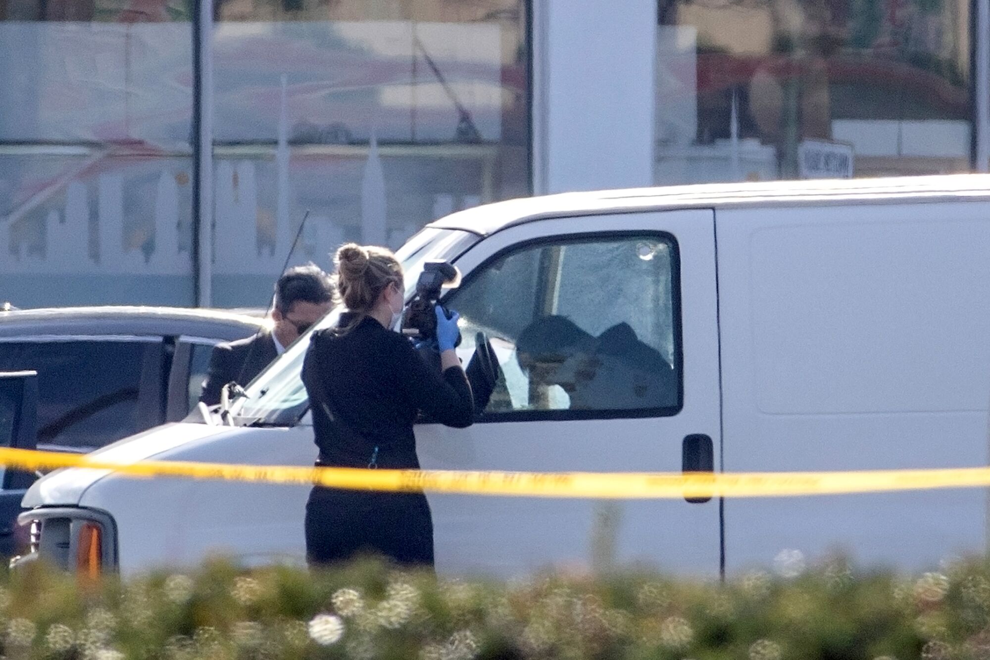 A coroner official takes photos of a man slumped over the steering wheel of a white van.