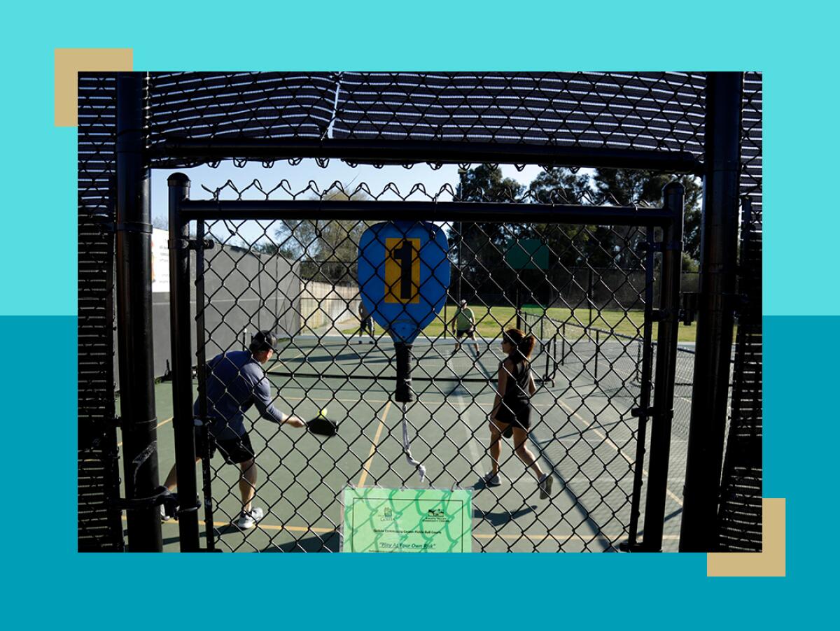 A paddle hangs on the fence of a pickleball court where people are playing.
