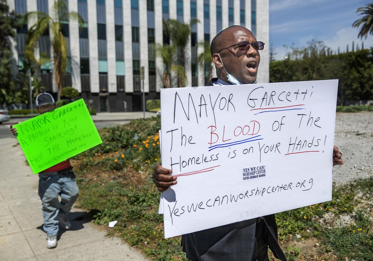Miguel Rios, left, who is homeless, and Pastor Sherman Manning carry protest signs along Wilshire Boulevard in L.A.