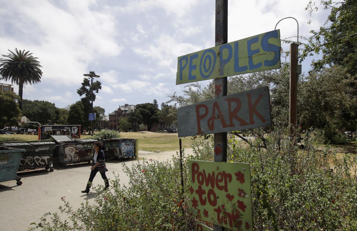 A woman walks behind a sign for People's Park.