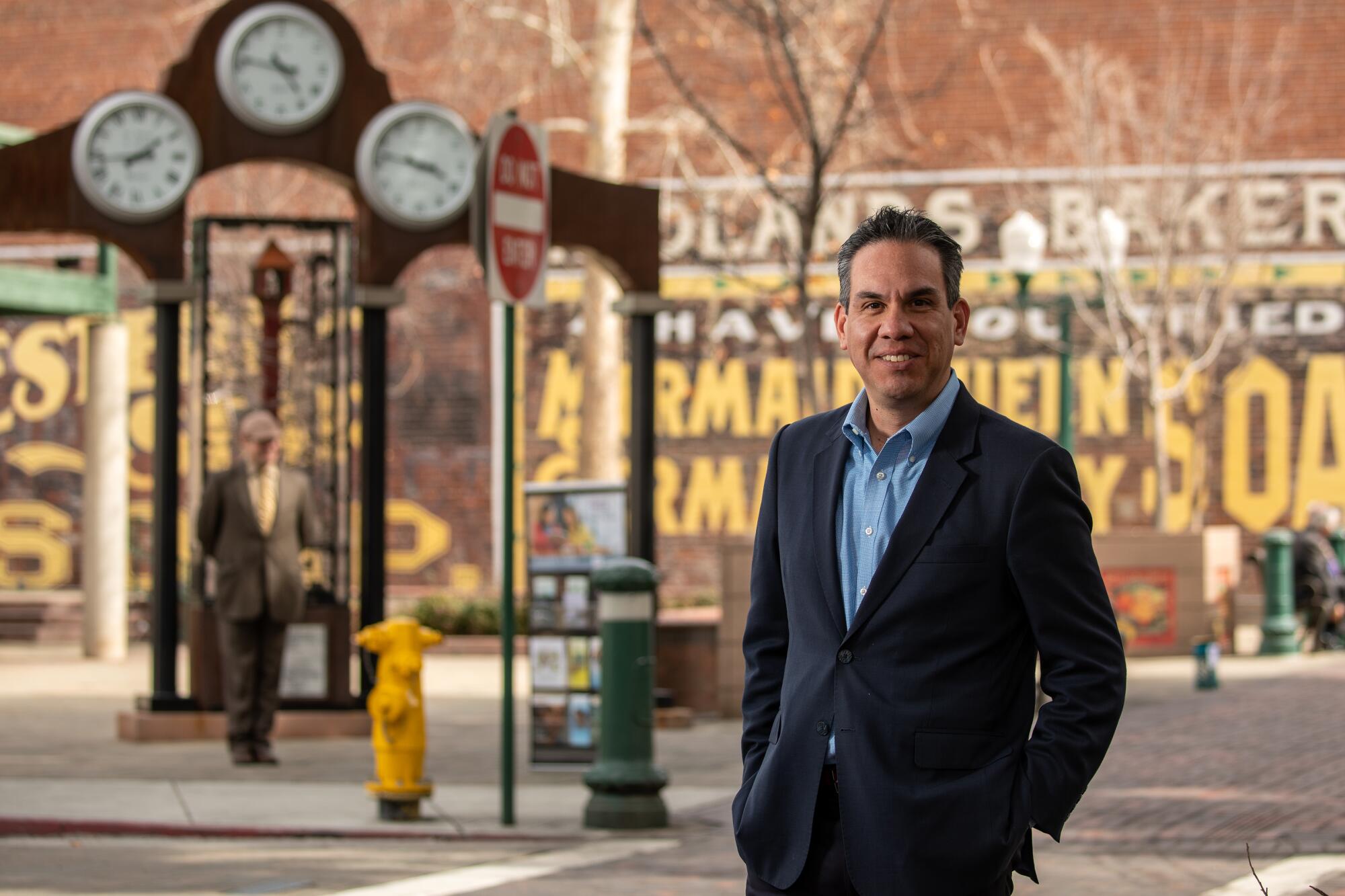 Rep. Pete Aguilar, stands for a portrait outdoors, with a street scene behind him.