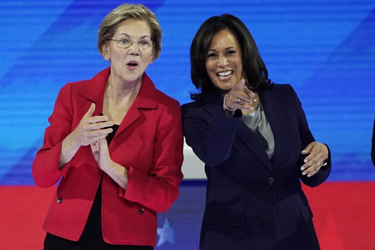 Two women on a red and blue debate stage, one clapping as the other points into the audience