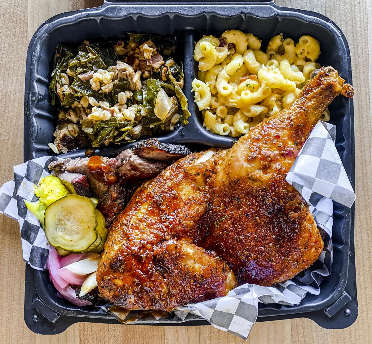 A takeout container with barbecued chicken, collard greens and macaroni and cheese.