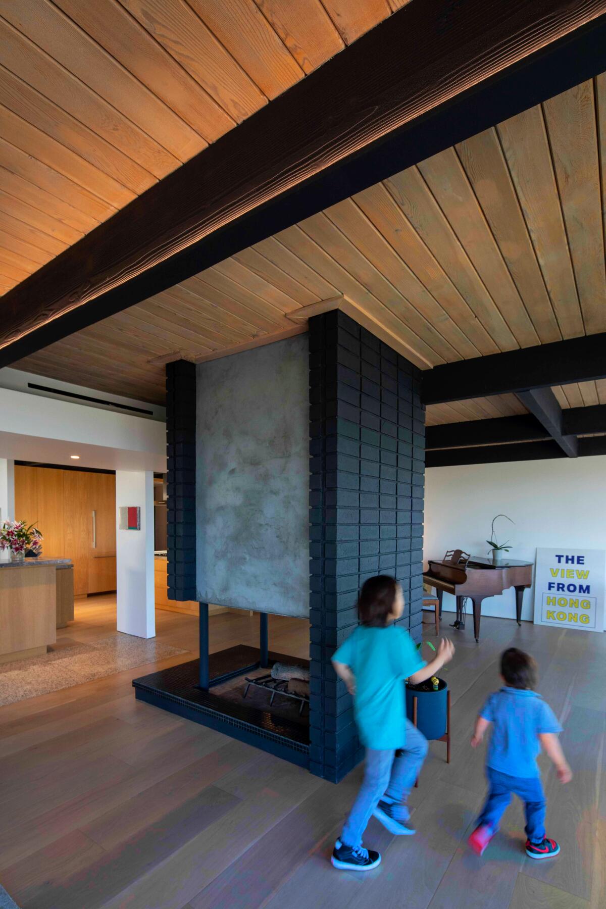 Two young boys run around a free-standing fireplace in a house.