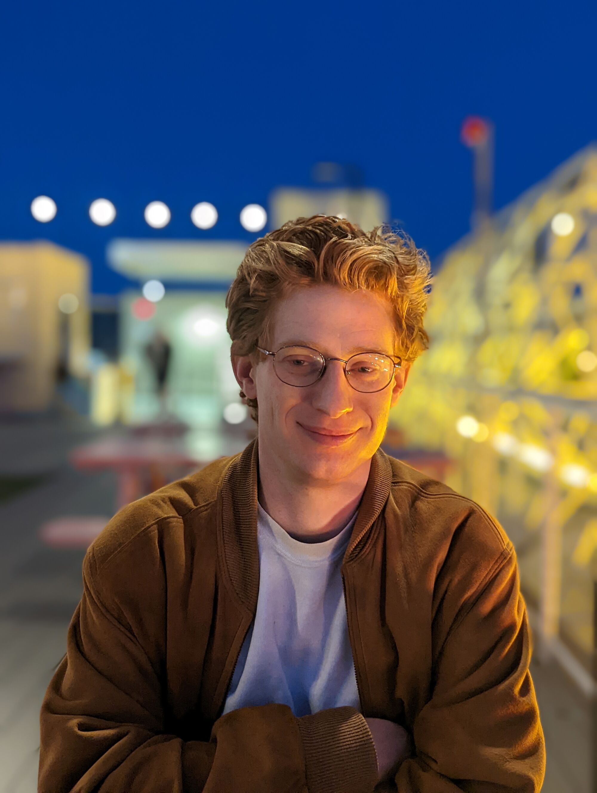 A man wearing glasses, a jacket and a T-shirt, smiling.