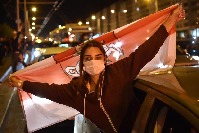 A woman wearing a face mask holds the former white-red-white flag of Belarus during a protest rally against police violence during recent rallies of opposition supporters, who accuse strongman Alexander Lukashenko of falsifying the polls in the presidential election, in Minsk on August 13, 2020. - Thousands of protesters formed human chains and marched in Belarus on August 13, 2020, in a growing wave of peaceful demonstrations over President Alexander Lukashenko's disputed re-election and an ensuing brutal police crackdown. Belarusian President has ordered an investigation into the mass detention of protesters and more than 1,000 have been freed, a senior politician said on August 13. (Photo by Sergei GAPON / AFP) (Photo by SERGEI GAPON/AFP via Getty Images)