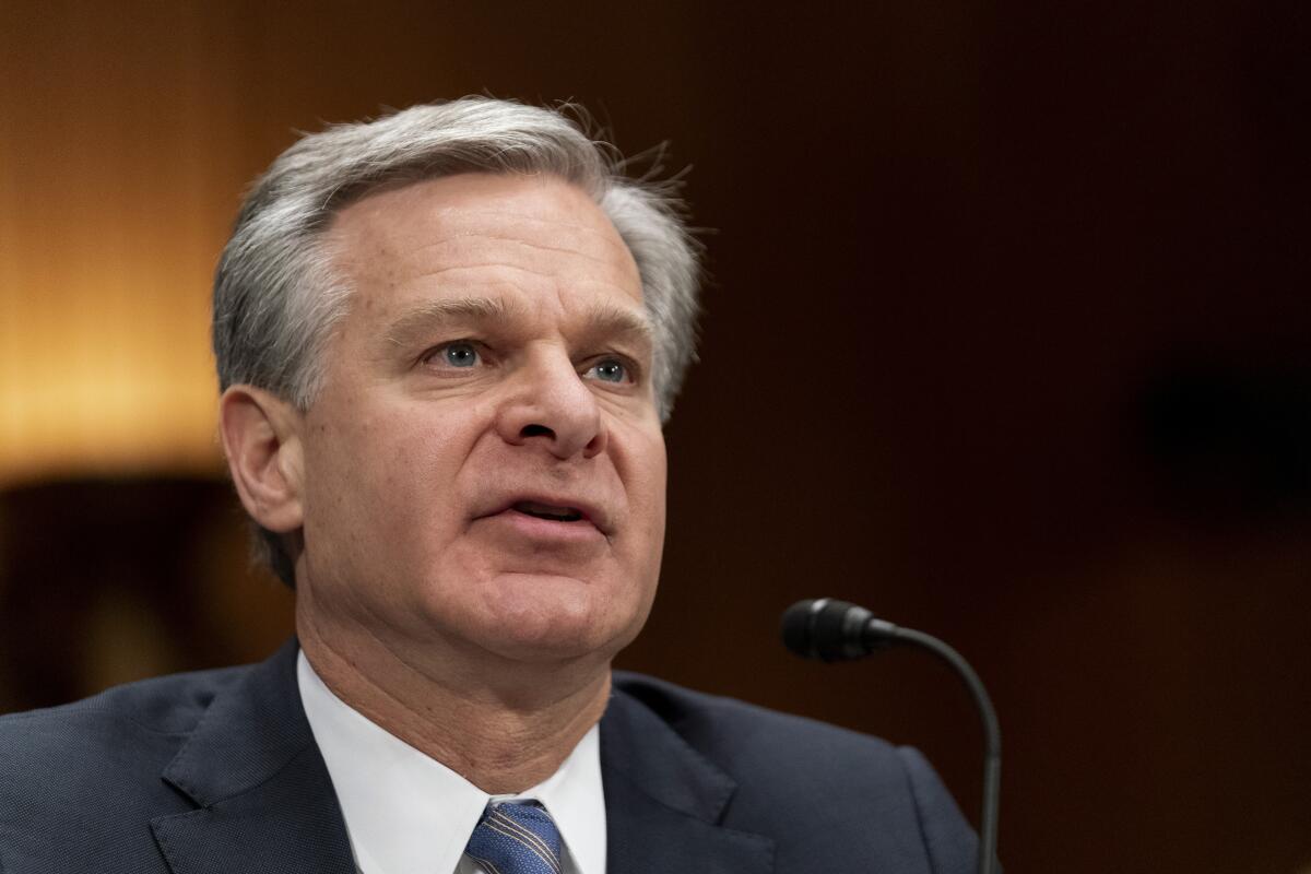 FBI Director Christopher A. Wray pictured from the shoulders up, speaking into a small microphone.