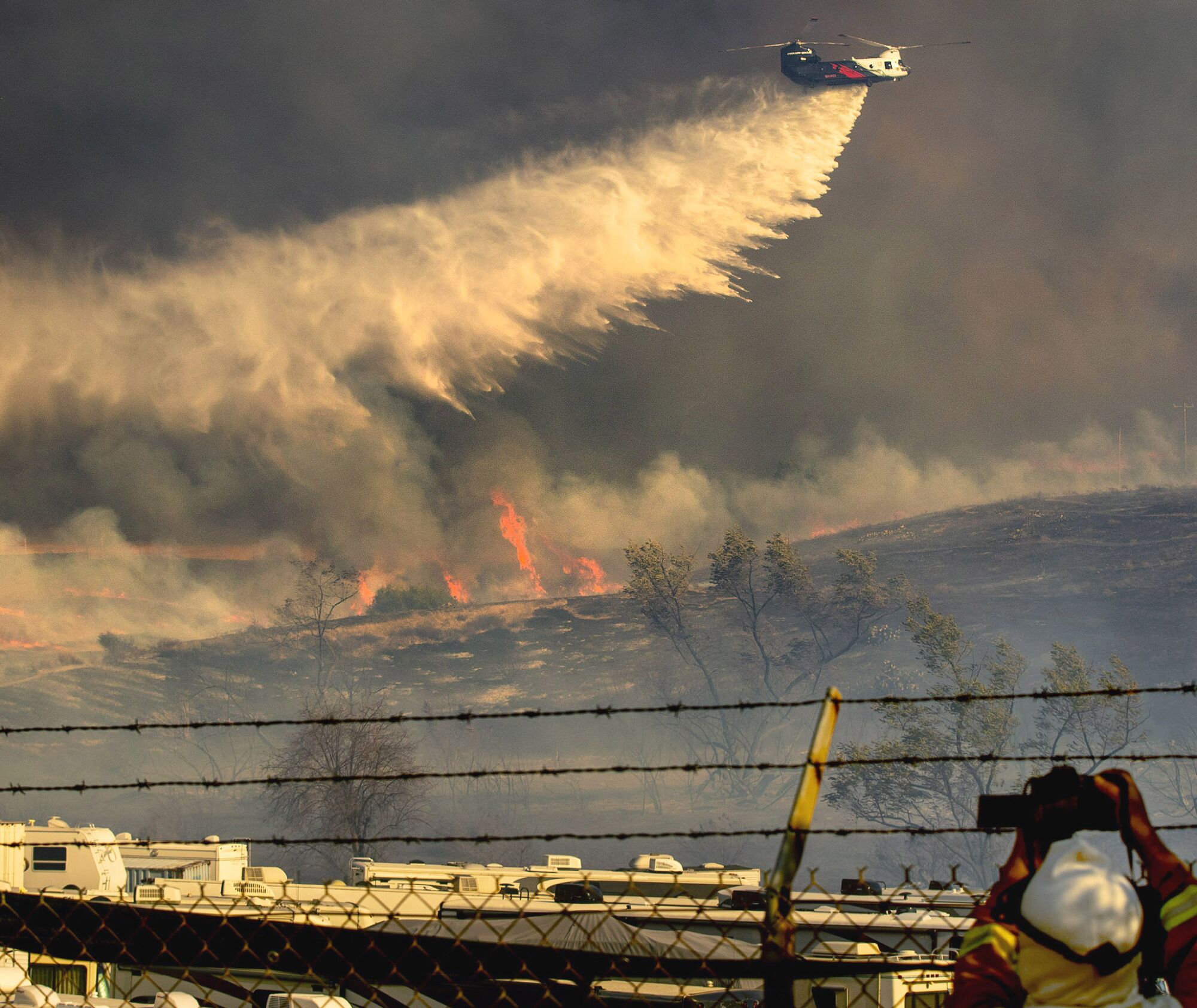 Water falls from a helicopter over flames and smoke