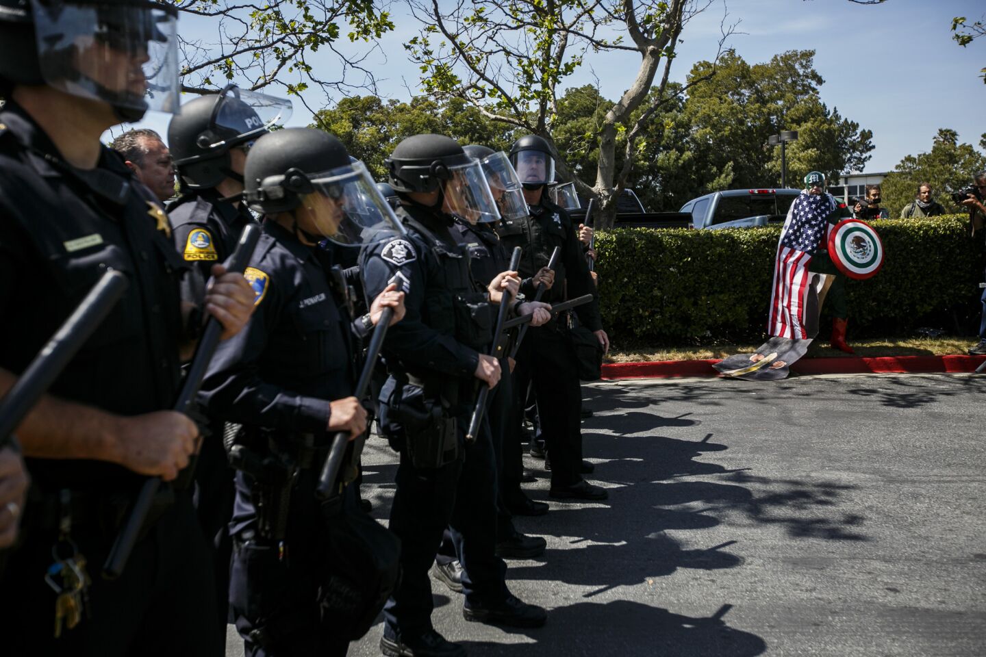 An anti-Trump protester dressed in a costume meant to parody Captain America watches as police hold a skirmish line at the California Republican Party convention in Burlingame in April 29, 2016.
