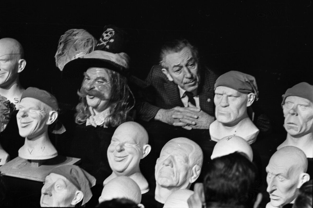 Walt Disney is surrounded by plastic heads