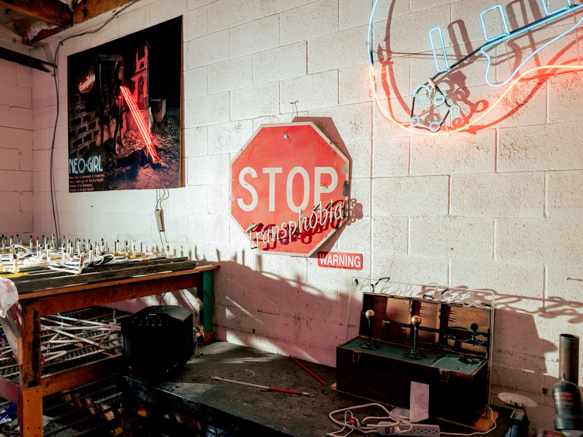 A neon art piece by Roxy Rose, reading "Stop Transphobia," hangs on the wall of her workshop.