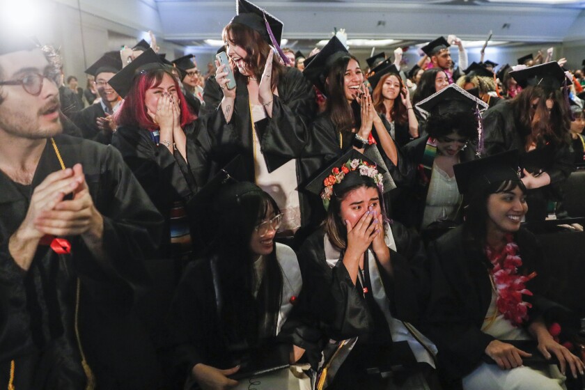A crowd of cheering graduates in black gowns and square academic hats