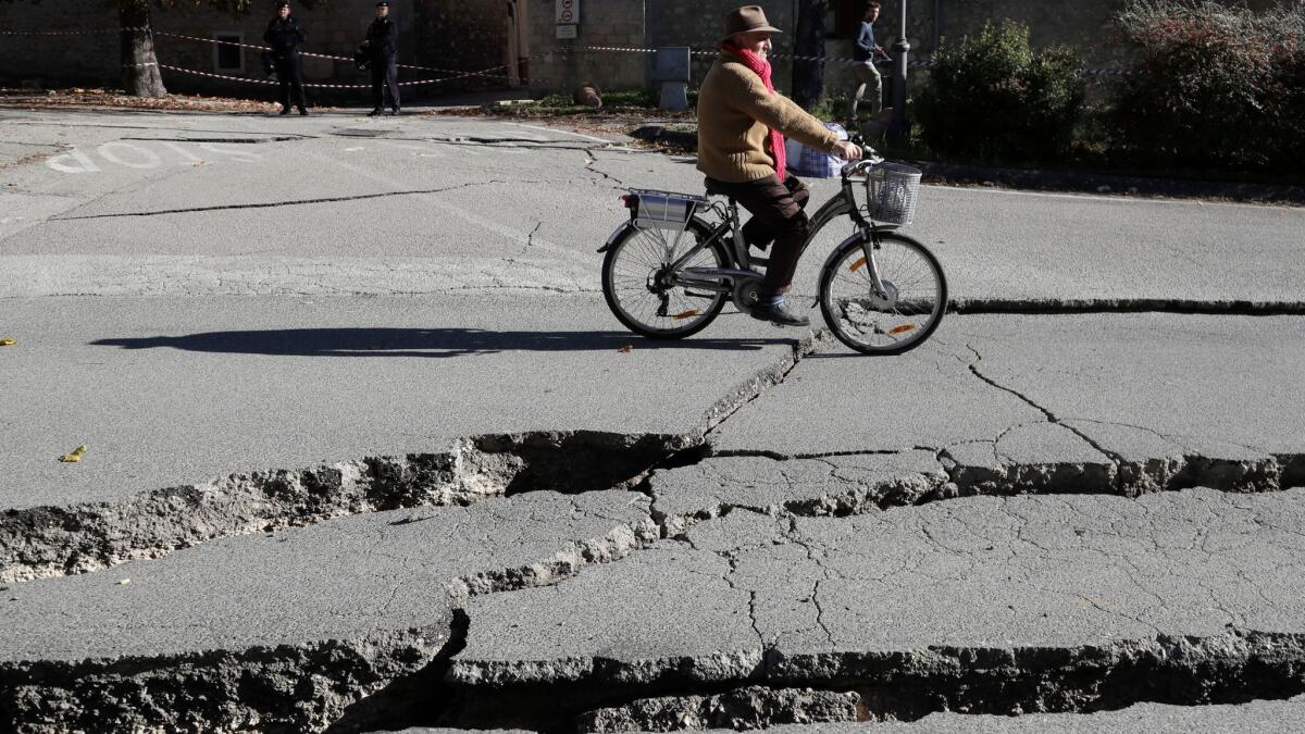 A man rides past cracks in a road in Norcia, central Italy, after an earthquake with a magnitude of 6.6 hit on Sunday.
